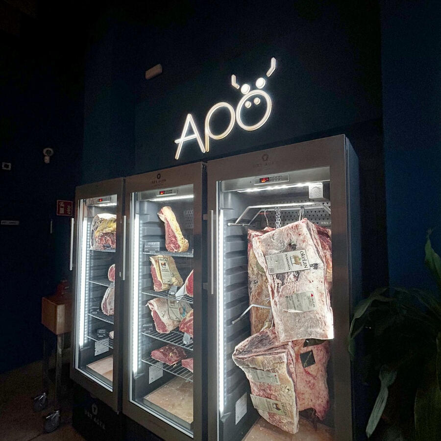 Cámaras de maduración Dry Ager de Apö con piezas de distintas razas de vacuno mayor etiquetadas, bajo el logo del restaurante en Granada
