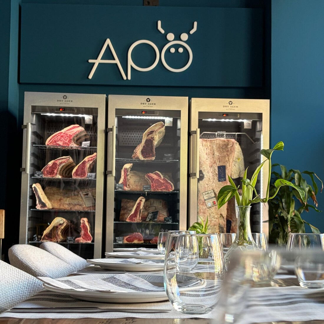 Sala de Apö en Granada con la mesa puesta y las cámaras de maduración Dry Ager al fondo, lista para una comida de empresa