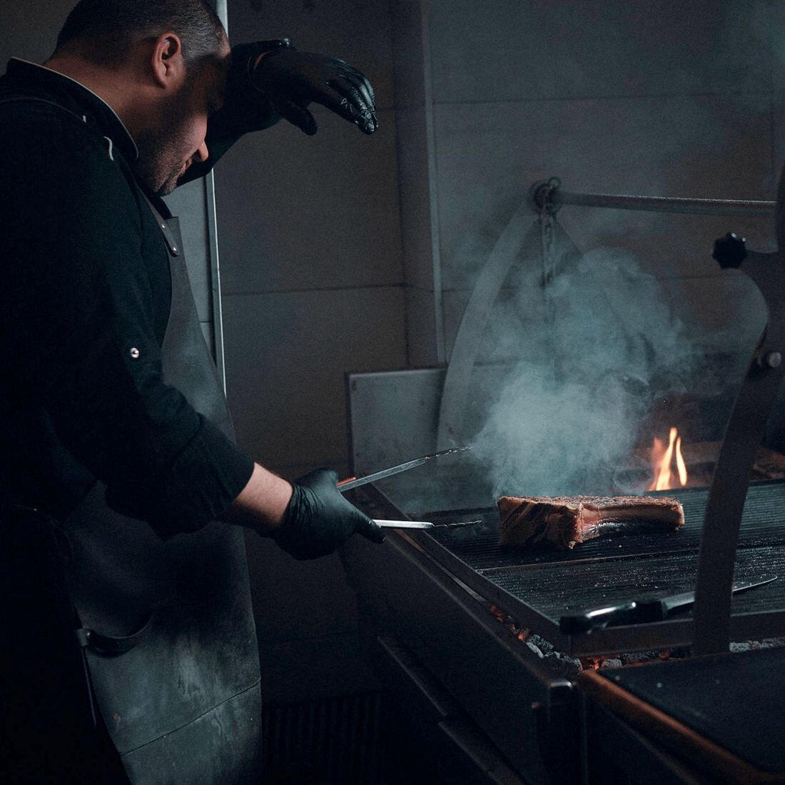 Parrillero trabajando junto a la brasa abierta del asador Apö en Granada